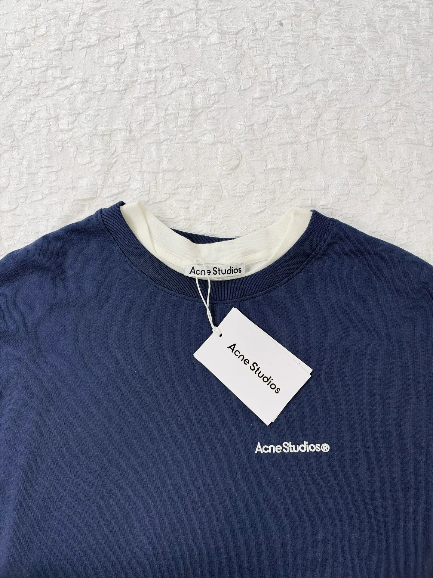 Acne Studio letter logo embroidered fake two-piece deconstructed long-sleeved T-shirt. Made of 100% cotton knitted plain fabric. The garment is pre-shrunk and washed to effectively reduce washing shrinkage. The version adopts dropped shoulder sleeves + loose box cut, the round neck is equipped with a rib collar, and the binding strip is used under the collar for reinforcement. The front chest uses high-density computer embroidery technology to present the brand logo. Visually, the inner and outer layers are designed with contrasting color splicing. The hem and cuffs are double-layered fake two-piece stacking. The sewing adopts flat seam + overlock technology. The lines are even and dense, and the overall relaxed silhouette takes into account practical wearability and layering effect. It can be worn alone or layered. Size：S/M/L/XL